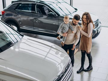 Eine Familie erkundet bei Autoankauf Augsburg und bewundert ein weißes Fahrzeug, während ein stilvoller SUV im Hintergrund in einem modernen Showroom zu sehen ist.